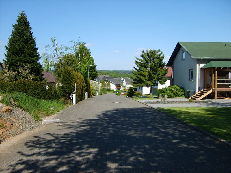 Wohnstraße in Stahlhofen am Wiesensee mit Häusern, Bäumen und Blick auf bewaldete Hügel